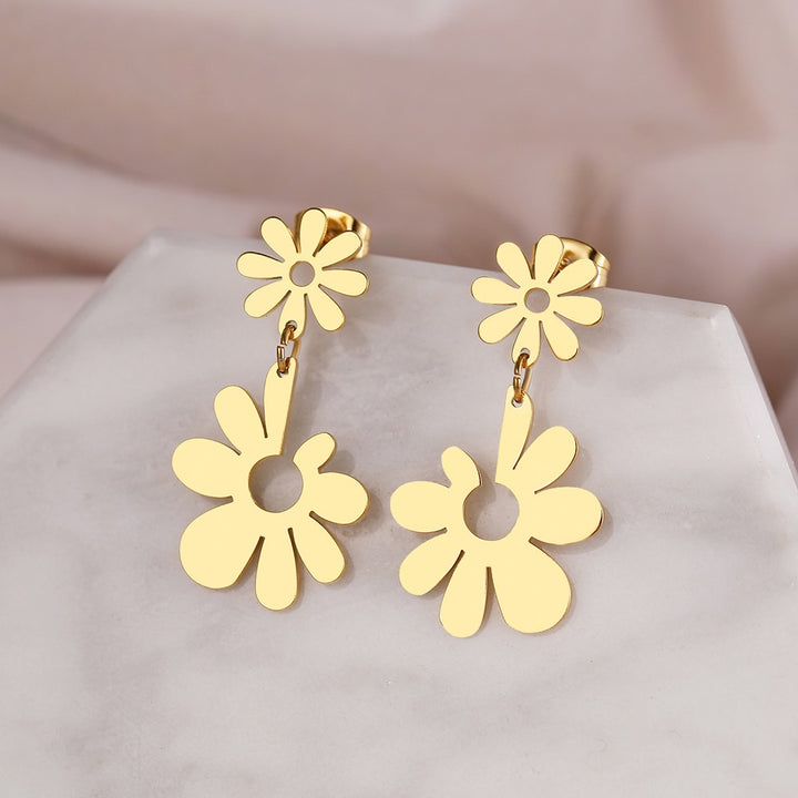 Boucles d'oreille pendantes avec double fleur marguerite en acier inoxydable plaqué or ou argent. Pétales réguliers et variés pour une touche florale raffinée.