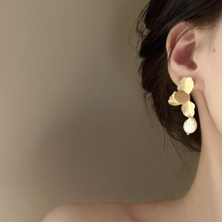 Une femme portant des boucles d'oreille en or avec des pétales de fleur et une perle ronde plate - une touche de grâce intemporelle pour toute tenue féminine.