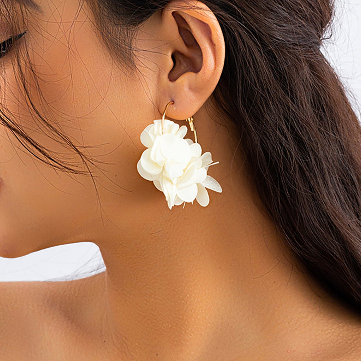 Une femme porte des boucles d'oreille créoles dorées avec de ravissantes fleurs en tissu. Ajoutez une touche florale à votre tenue avec ces bijoux féminins et élégants. Parfaites pour les amoureuses de la nature et de la mode. Boucle d'oreille créole fine dorée fleurs pendantes tissu - Femme.