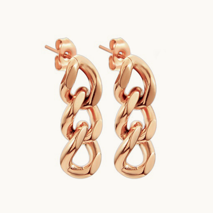 Une paire de boucles d'oreilles est exposée devant un fond beige. Elles sont plaqué or rose et sont constituées de 3 maillons de chaînes de style gourmette. 