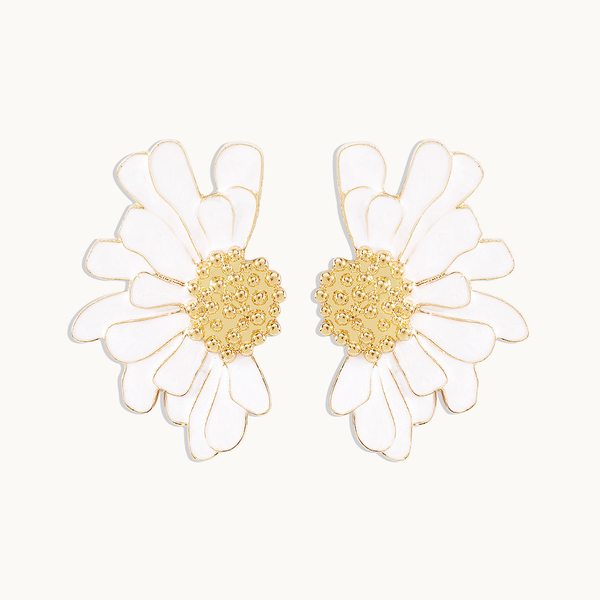 Une paire de boucles d'oreilles est exposée devant un fond beige. Ce sont deux demies fleurs imposantes avec le coeur de la fleur doré et les pétales blancs. 