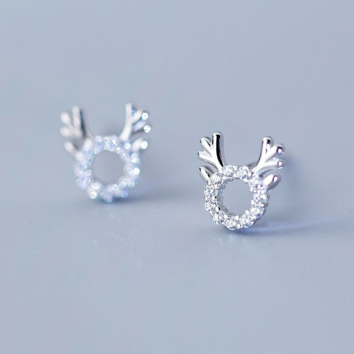 Une paire de boucles d'oreille argentées avec des diamants, ornées de bois de renne argentés sur le dessus. Parfaites pour les festivités de Noël.