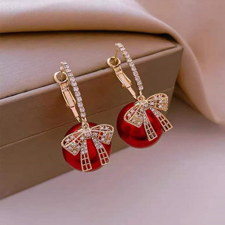 Une paire de boucles d'oreille dormeuses avec des nœuds rouges et dorés - Bijoux de Noël féeriques pour illuminer votre look festif.