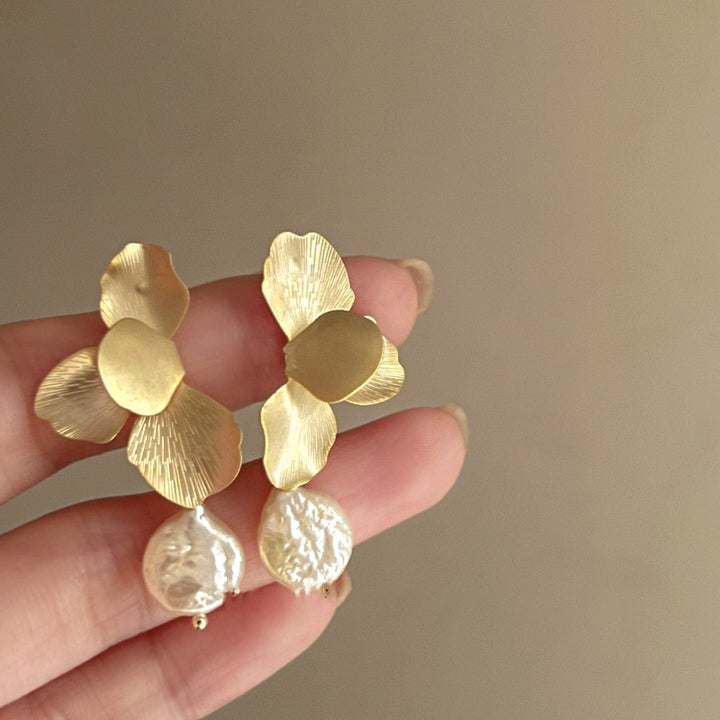 Une main tenant une paire de boucles d'oreille pendantes en pétales de fleur avec perle ronde plate en cuivre doré ou argenté - Femme.